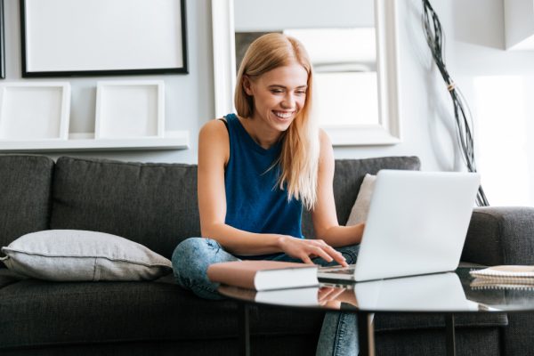 happy-woman-sitting-on-sofa-and-using-laptop-at-home